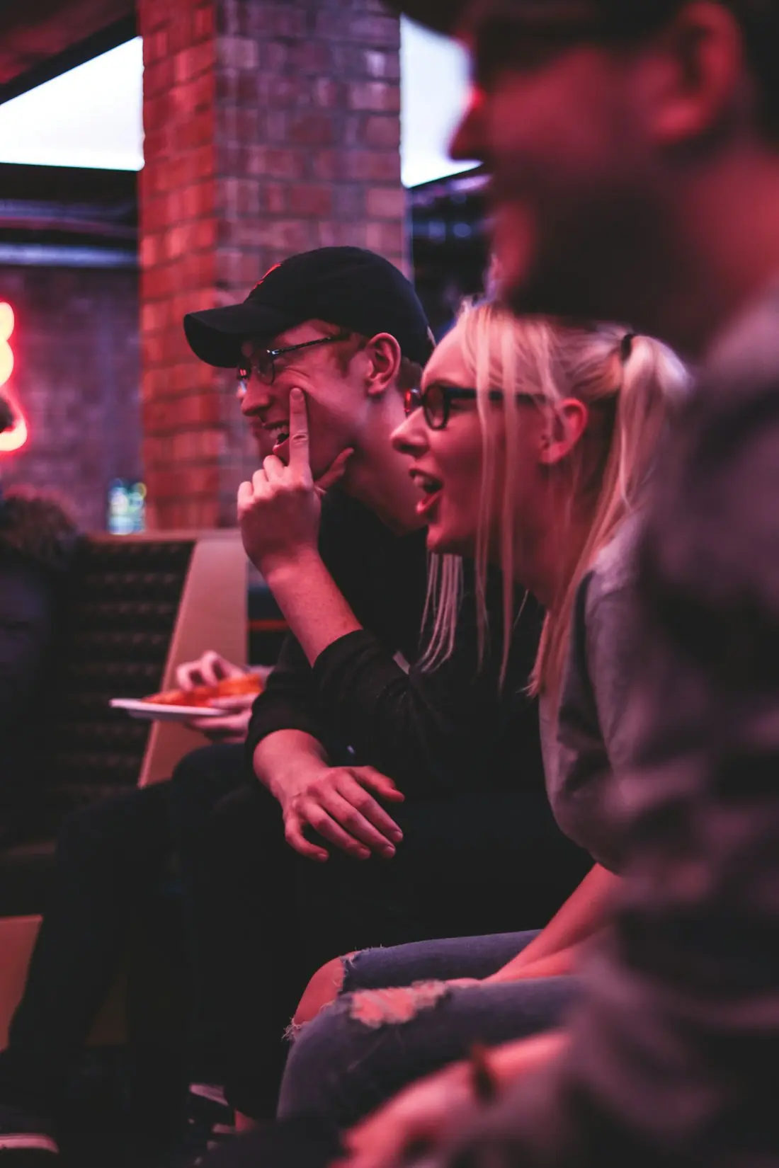 Friends in a dim bar leaning in mid-game, one thinking with a finger to his chin